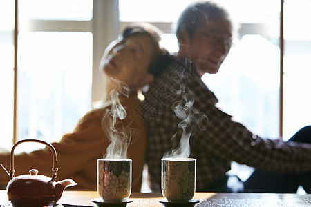 起居室茶桌旁背靠背坐着的老年夫妻图片