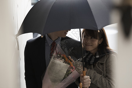 女孩对着打着伞拿着花的男友微笑图片