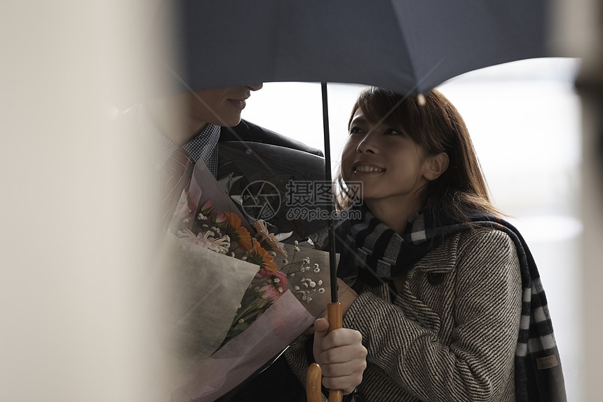 女孩对着打着伞拿着花的男友微笑图片