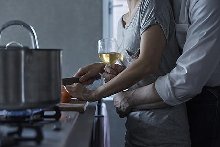 端着酒杯的男人搂着切菜的女人背景图片