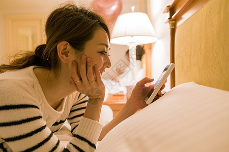 女人穿着睡衣趴在床上玩手机图片