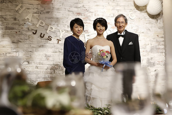 拿着捧花的新娘站在父母中间看着镜头微笑图片