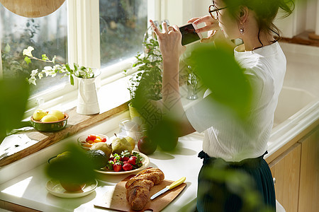在窗边料理台制作午饭拍照的女人图片