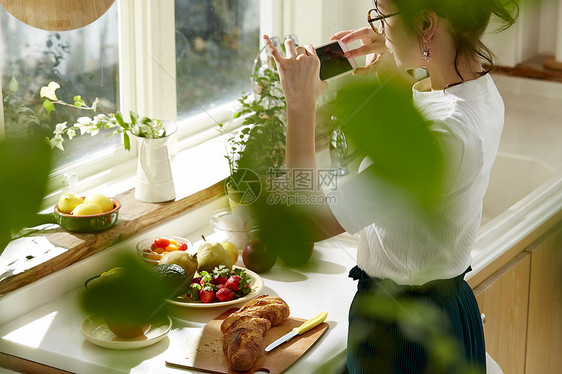 在窗边料理台制作午饭拍照的女人图片