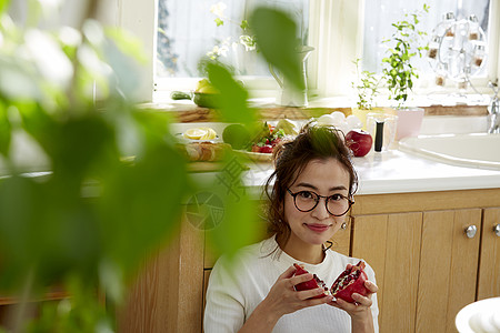 在窗边料理台蹲下看切开的石榴的女人图片