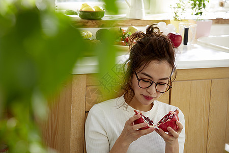 在窗边料理台蹲下看切开的石榴的女人图片