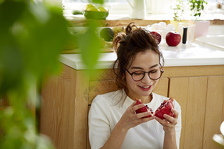 在窗边料理台蹲下看切开的石榴的女人图片