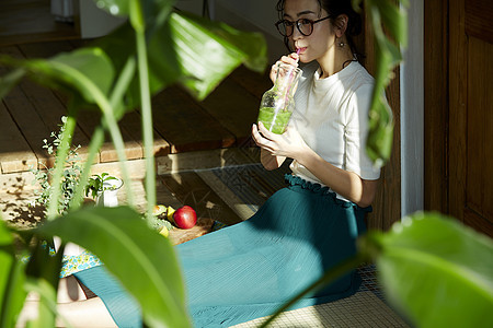 坐在木地板上晒着太阳喝奶昔的女人图片