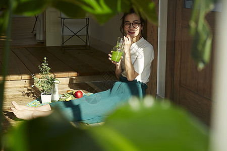 坐在木地板上晒着太阳喝奶昔的女人图片