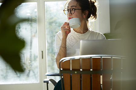 女人坐在窗边的桌上喝咖啡工作图片