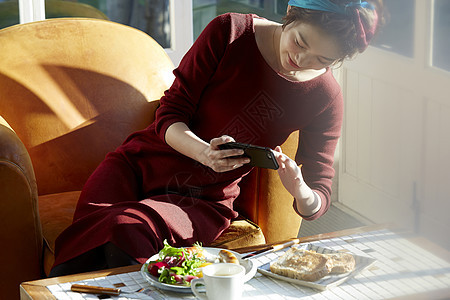 女人拿着手机给桌上的食物拍照图片