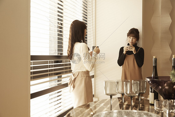 在公寓窗边和朋友喝酒聊天的女人图片