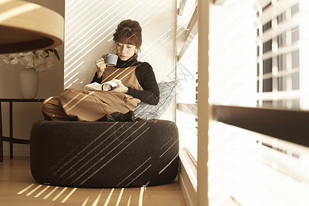 坐在公寓窗边沙发上看书喝咖啡的女人图片