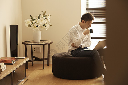 男人坐在沙发上喝咖啡用电脑工作图片