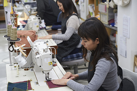缝纫工厂车间在制作手提包的女缝纫工背景