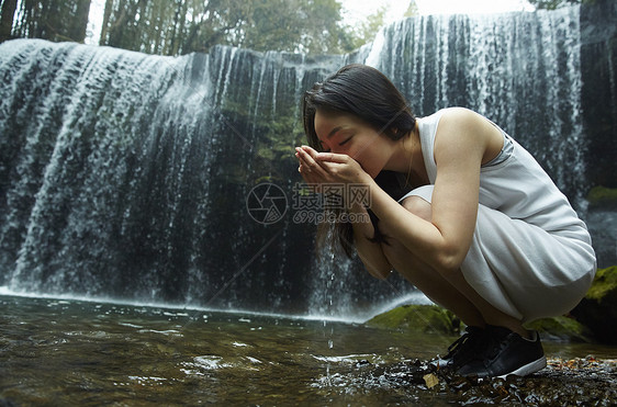 站在小溪边享受瀑布的女人用手捧水喝图片