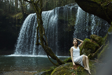 坐在小溪边享受瀑布的女人抬头看图片