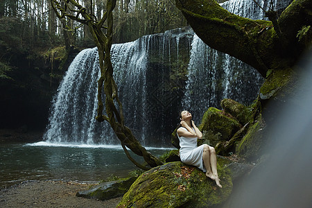年轻女性坐在小溪旁的岩石上放松图片