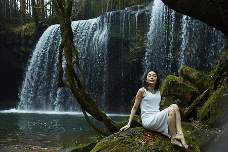 年轻女性坐在小溪旁的岩石上图片