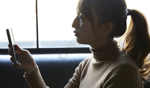 在窗边看手机思考的女性图片