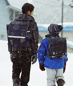 下雨天背着书包雪地里行走的学生背影图片