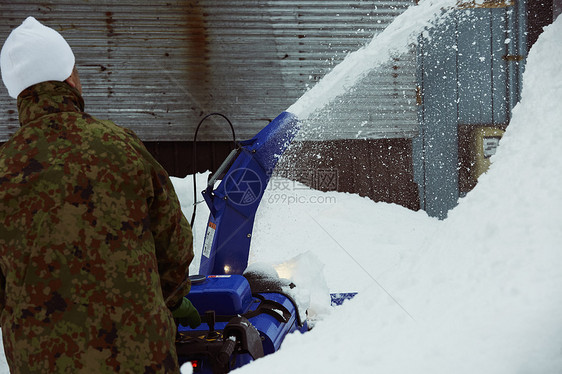 户外积雪使用除雪机的男性背影图片