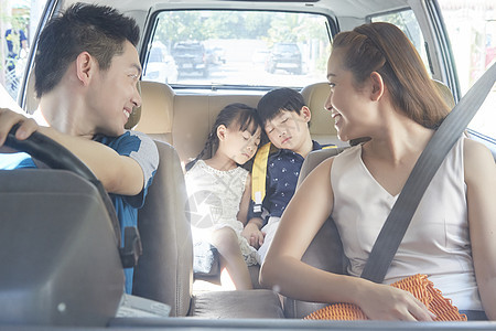 车中的父母回头看向在车后座上睡着的儿女背景图片