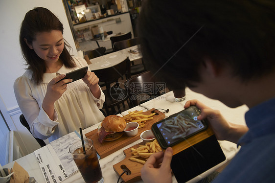 汉堡店内拍摄美食的情侣图片