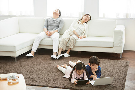 趴在地上玩电脑的小孩和沙发上疲惫的父母图片