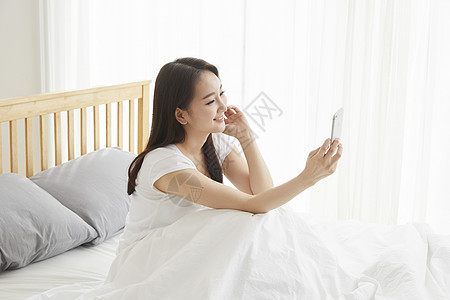 床上拿着手机视频通话的年轻女性图片