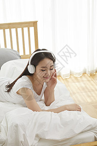 坐在床上带着耳机听音乐放松的女性图片