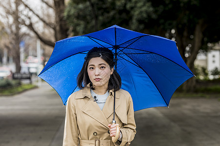 暴雨撑着雨伞站在街头的年轻女性图片