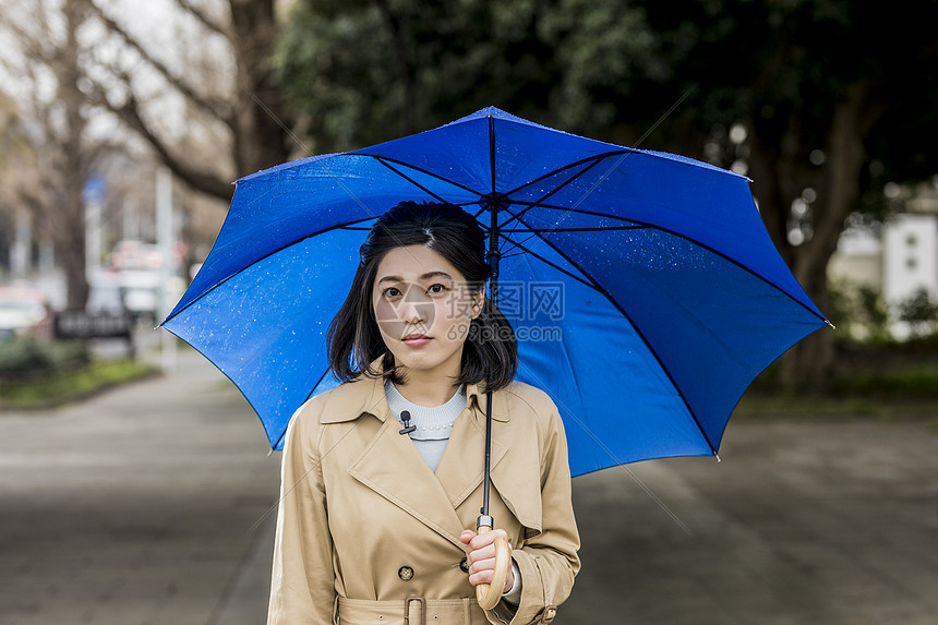 暴雨撑着雨伞站在街头的年轻女性图片