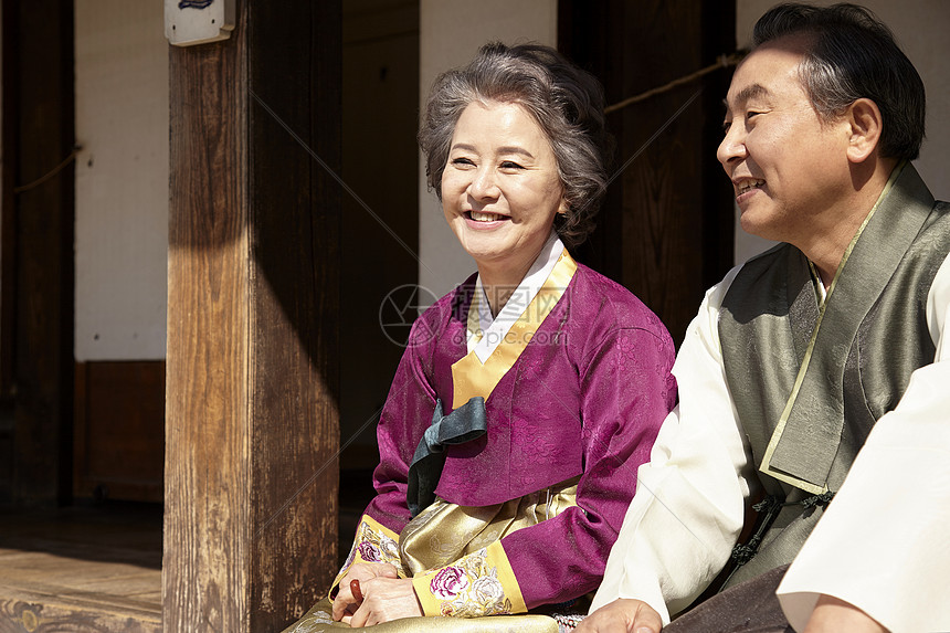 穿着传统服装坐在民俗屋前的老年夫妇图片