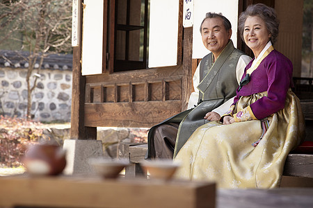 穿着传统服装坐在屋子前微笑的夫妇图片