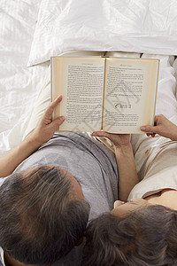 卧室里躺在床上看书的夫妇图片