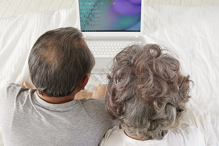 床上看笔记本电脑放松的老年夫妻背景图片