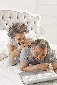 卧室里看着笔记本电脑放松开心的老夫妇图片