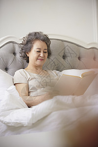 坐在床上看书的老年女性背景图片