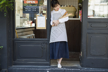 咖啡馆门口年轻女子抱着新鲜出炉的法式面包图片