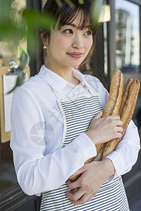抱着新鲜出炉的法式面包微笑的女性图片