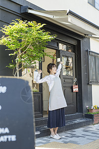 咖啡馆门口穿着围棋伸懒腰的年轻女性图片