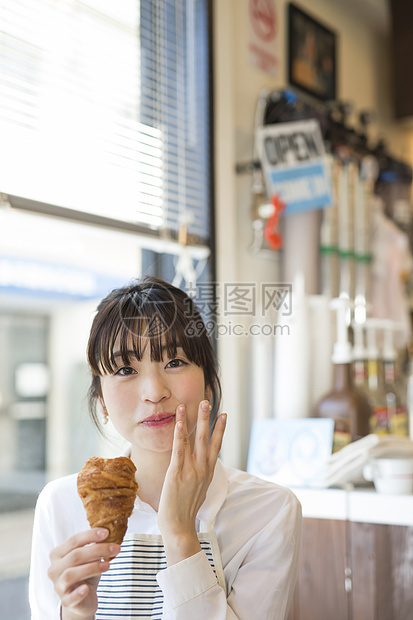 咖啡馆吃着面包微笑的年轻女性图片