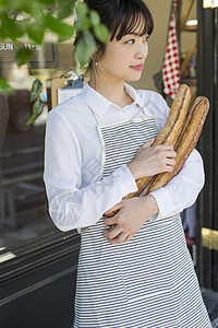 门口抱着新鲜出炉的法式面包的青年女性图片