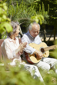 公园长凳上放松弹吉他的老年夫妇图片