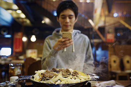 餐馆里拿着手机拍摄食物照片的男性图片
