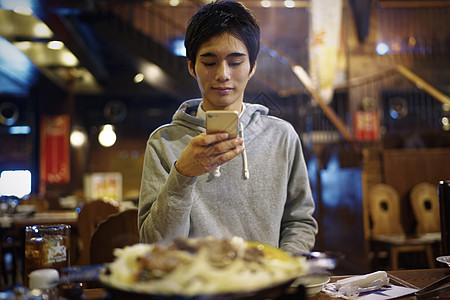 餐馆里拿着手机拍摄食物照片的男性图片