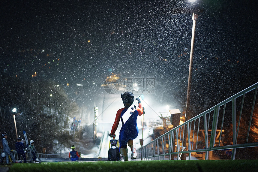 夜晚滑雪场拿着滑雪板的运动员背影图片