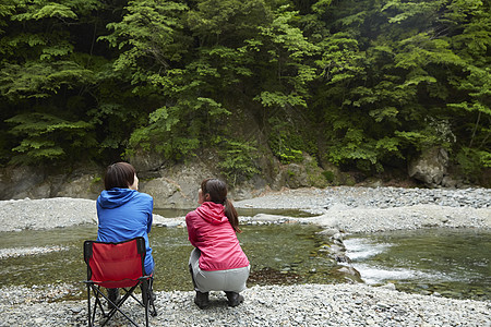蹲下的人背影两个女人在河岸边放松享受自然背景