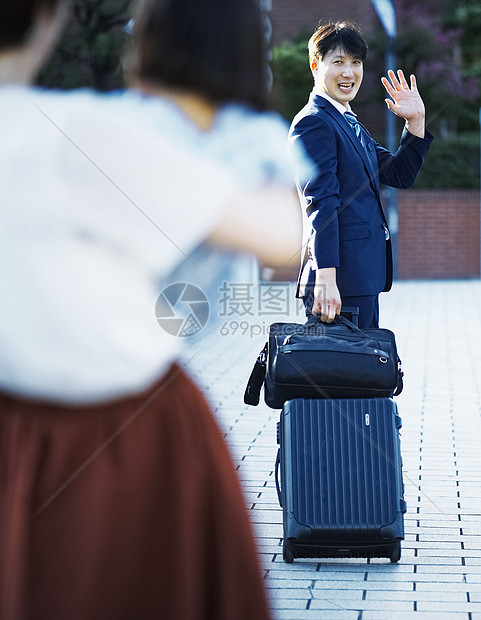 穿着西装拉着行李箱与家人告别的成年男子图片